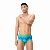 Speedo men's printed 13.5cm brief featuring quilt triangle design in blue and green, made from quick-drying swimwear fabric.