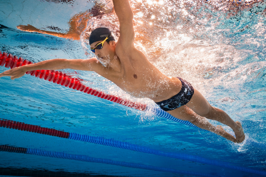 Swimmer wearing a chlorine-resistant training swimsuit beside an indoor swimming pool.