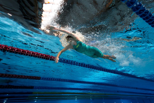 Competitive swimmer wearing a race suit swimming underwater in a lane pool.