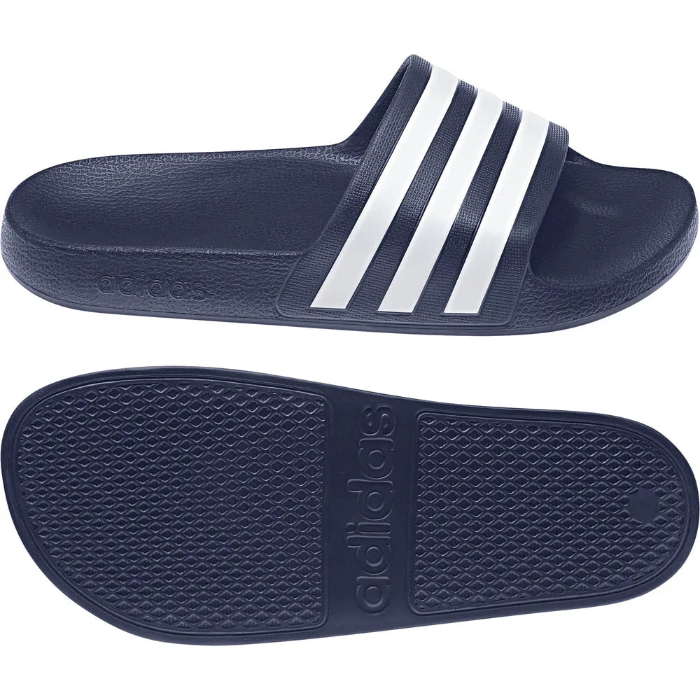 Navy blue Adidas Adilette Aqua slides on a tiled floor, showing the sporty slide design and Adidas logo on the strap.