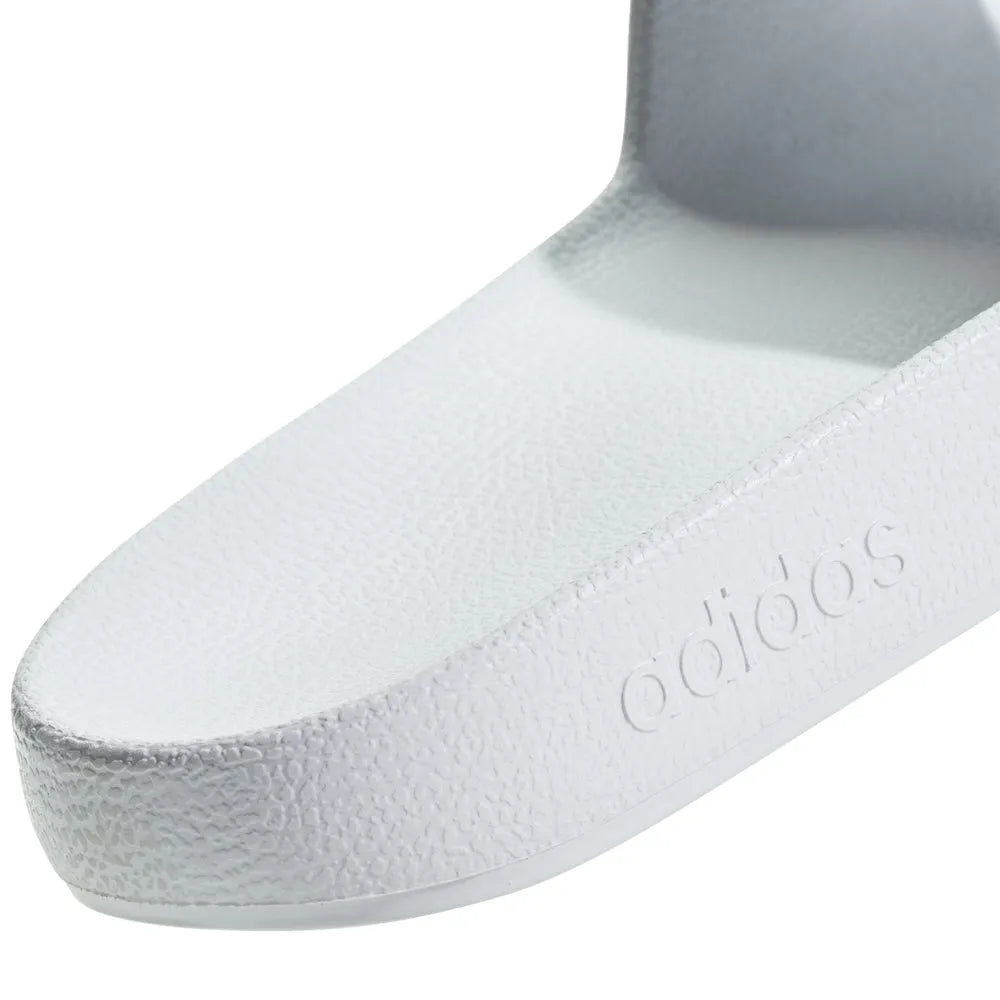 White Adidas Adilette Aqua Slides on a flat surface, showcasing their sleek design and sporty style.
