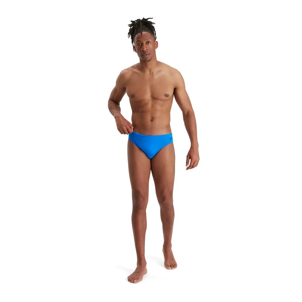 Blue Speedo Eco Men's Endurance+ 7cm Briefs, close-up view showing comfortable fit and elastic waistband in a swimming pool setting.