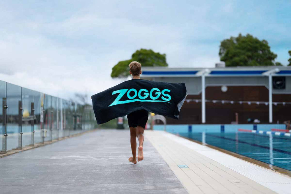 Zoggs black and turquoise swimming pool towel spread out, featuring soft fabric and Zoggs branding for poolside comfort.